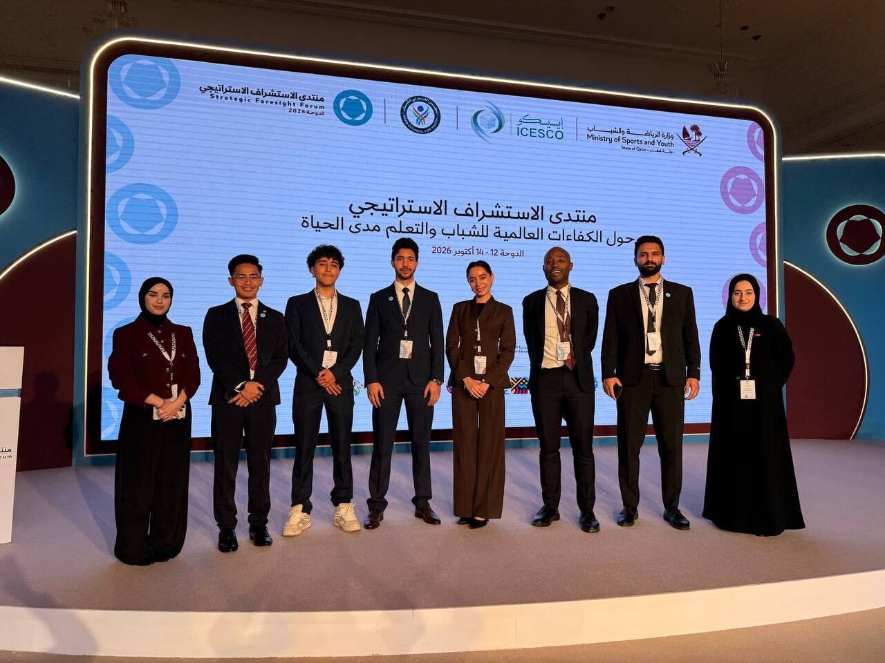 Eight delegates standing in front of the Strategic Foresight Forum backdrop in Doha, which carries the logos of the Arab Council for Youth, ICESCO and the Ministry of Sports and Youth of the State of Qatar above the forum title and the dates 12–14 October 2026.